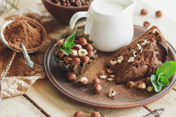 Piece of chocolate cake, mint leaves, hazelnuts and jar with milk