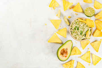 Homemade guacamole in bowl, served with tortilla nachos lime lemon and parsley, with half of avocado on white concrete table. Copy space