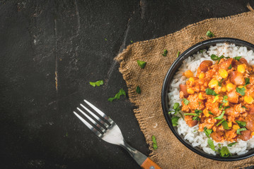 Traditional Mexican Chilean food, chili con carne, served in a portioned bowl with rice. On black concrete table, top close view copy space