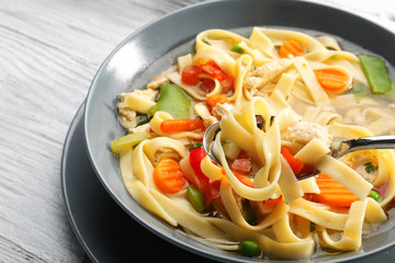 Spoon with chicken noodle soup over plate, closeup