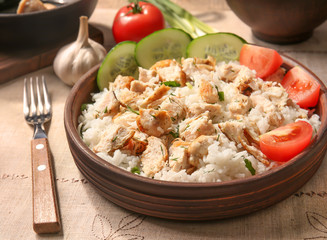 Delicious rice with chicken and vegetables in bowl on table