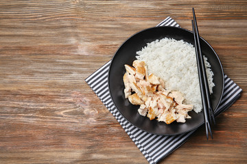 Black plate with delicious chicken and rice on wooden table
