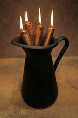 Christmas decoration for advent with four brown candles in black metal pitcher.