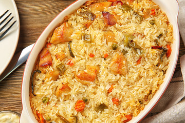 Tasty rice with chicken and vegetables in baking dish on kitchen table