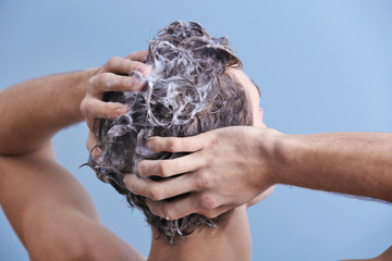 Young man washing hair on color background