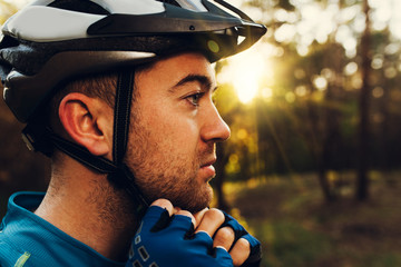 Close up portrait in profile of handsome and serious cyclist close his protective helmet outdoors...