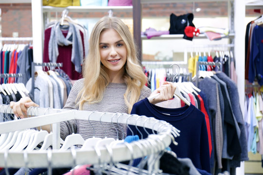 Beautiful young woman choosing clothes in modern shop