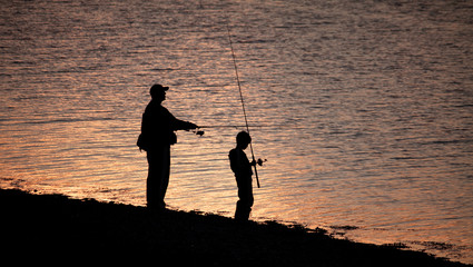 Silhouettes of father and son fishing on the lake in sunset