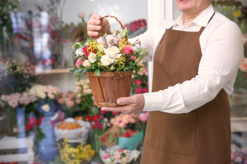 Male florist holding basket with flowers in flower shop