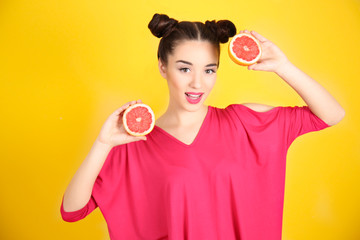 Beautiful young woman with grapefruit halves on yellow background