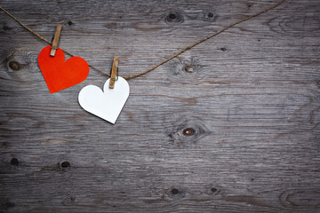 Two paper hearts Valentines red and white hanging on the rope on the clothespin. Wooden background texture