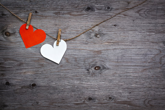 Two paper hearts Valentines red and white hanging on the rope on the clothespin. Wooden background texture