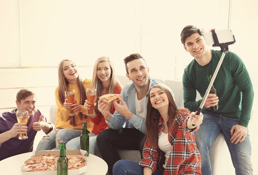 Friends taking selfie while eating pizza at home party