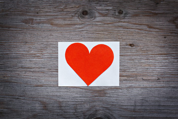 Red paper heart valentine on a white sheet of paper. Wooden background texture