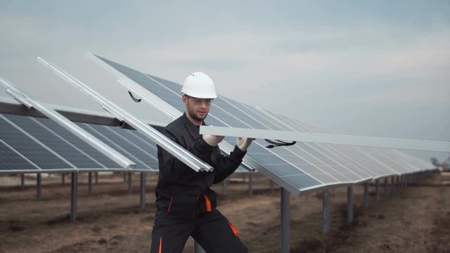Two workers in a uniform and hardhat install photovoltaic panels on a metal basis on a solar farm