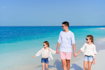 Father and little girls walking on white sandy beach
