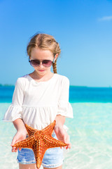 Adorable little girl with starfish on white empty beach
