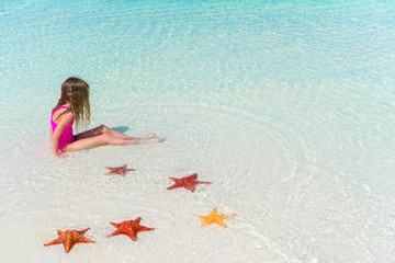 Fototapeta na wymiar Adorable little girl with starfishes in water on white empty beach