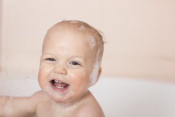 Cute smiling baby boy in a tub. Funny infant kid laughes and looking at camera