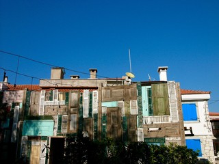 Verkleidete Fassade mit alten Holztüren und Fensterläden vor blauem Himmel im Sonnenschein in den...