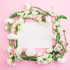 Frame of white ranunculus, snapdragon, tulip, lilac and freesia and paper card on pink background. Flat lay, top view. Floral frame