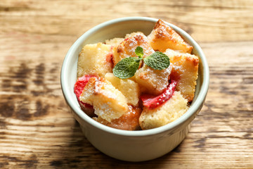 Delicious bread pudding with strawberry and mint in bowl on wooden table
