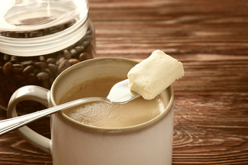 Cup of tasty butter coffee and shovel on wooden table, closeup