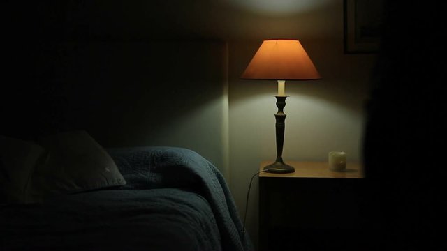Man prepares to go to bed and sleep. Person lays down in bed and turns off night stand besides bed
