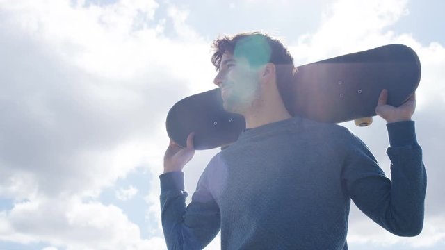 Young male holding his skateboard as he looks around, in slow motion