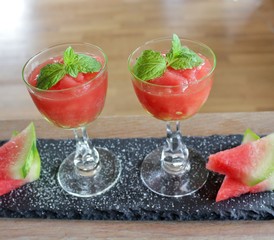 Tray with two glasses of watermelon granita decorated with mint leaves and slices of watermelon