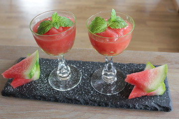 Tray with two glasses of watermelon granita decorated with mint leaves and slices of watermelon