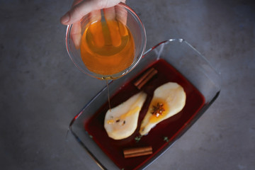 Female hand pouring honey on sliced pear in glass dish