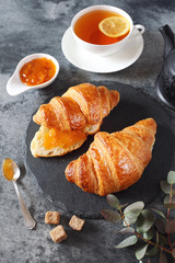 Two fresh croissants, jam, lemon tea and teapot