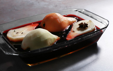 Pears with wine and spices in glass dish on table