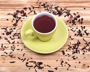 Wild berry tea in green cup with hibiscus leafs on wooden vintage background