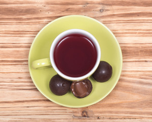 Wild berry tea in green cup with chocolate truffles on wooden vintage background