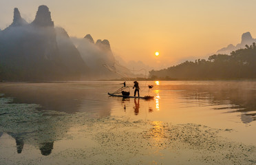 Cormorant fisherman throws a net with ancient traditional chinese bamboo boats at sunrise -...
