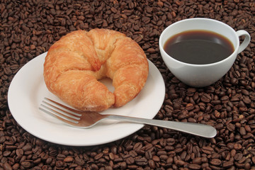 A white coffee cup with a pastry on a plat with fork on a background of coffee beans
