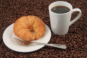 A white coffee cup with a pastry on a plat with fork on a background of coffee beans