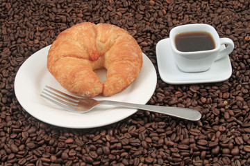 A white coffee cup with a pastry on a plat with fork on a background of coffee beans