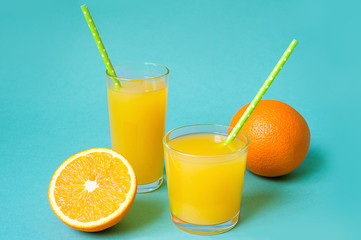 Glasses of orange juice with straw and slices on bright background