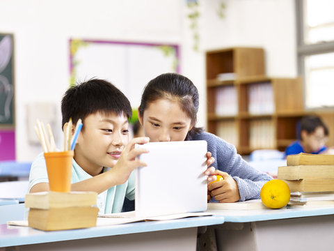 asian elementary school girl and schoolboy using tablet together