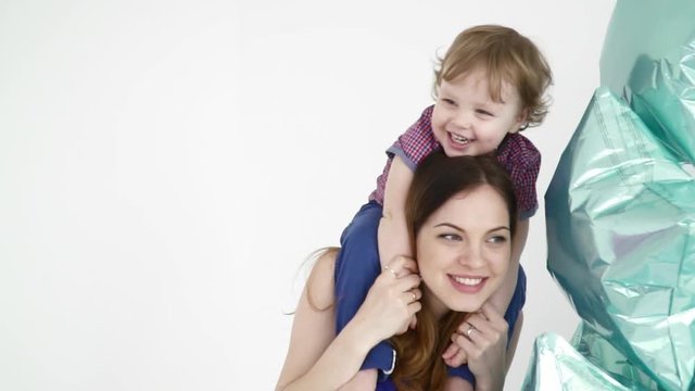 Beautiful mother holding her baby on her shoulders near the baloons closeup