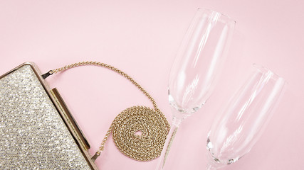 Festive evening golden clutch and two champagne glasses on pink. Holiday and celebration background. Luxury accessories and party concept