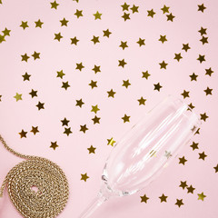 Festive evening golden clutch and champagne glass with star sprinkles on pink. Holiday and celebration background. Luxury accessories and party concept