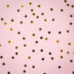 Golden star sprinkles on pink. Festive holiday background. Celebration concept