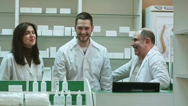 Three competent pharmacists laughing in a pharmacy looking at camera