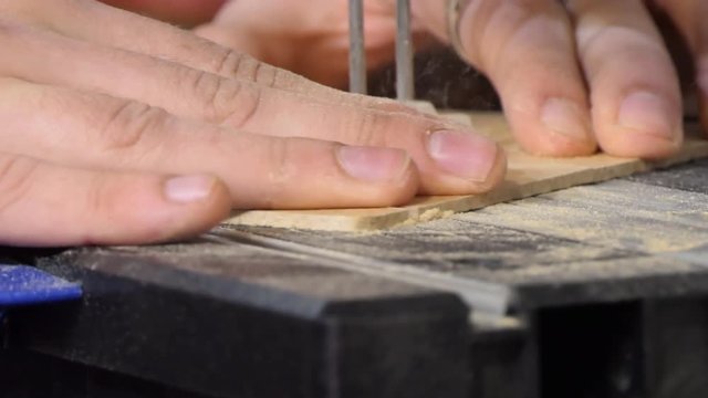 Close up of male hands holding piece of wood and cutting detail out of it using electric moto saw  