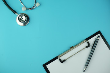 Top view of clipboard, sheet, pen and black stethoscope on blue background. Healthcare concept.