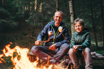 Father and son roast marshmallow candies on the campfire in forest